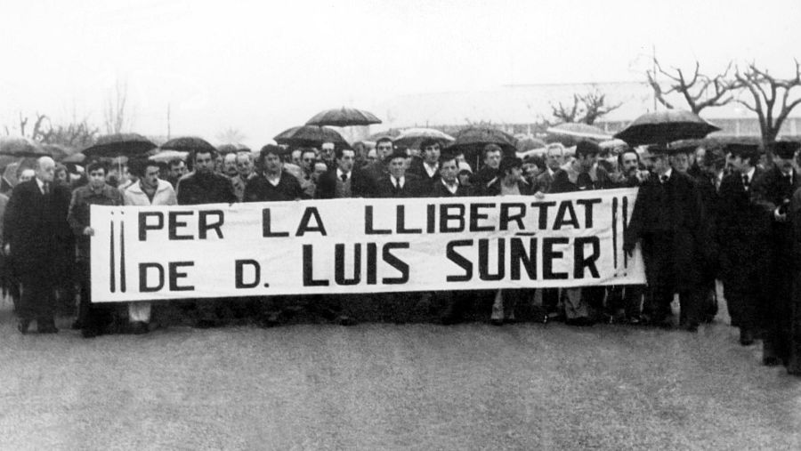 Multitud manifestándose bajo lluvia, con pancarta pidiendo la libertad de D. Luis Suñer. Fotografía en blanco y negro titulada "FOTO 07 OPERACION APOLO".