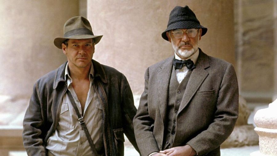 Imagen de Harrison Ford y Sean Connery en una escena de 'Indiana Jones y la última cruzada'.  Ambos actores, con atuendos de época, miran directamente a la cámara con expresiones serias.