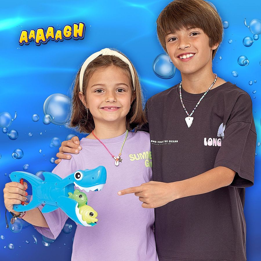 Niña y niño abrazados, bajo el agua (simulado), con un juguete de tiburón y peces. La niña lleva una camiseta lila y el niño una gris oscura, ambos con inscripciones.