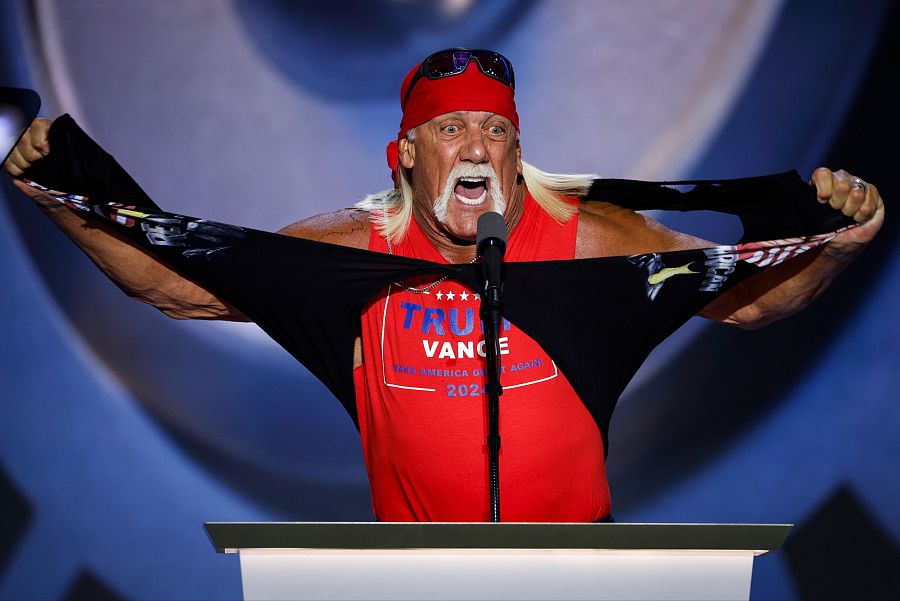Hulk Hogan, con bandana roja y gafas, rasga una camiseta para mostrar una con "TRUMP VANCE 2024".  Expresión eufórica en un escenario.