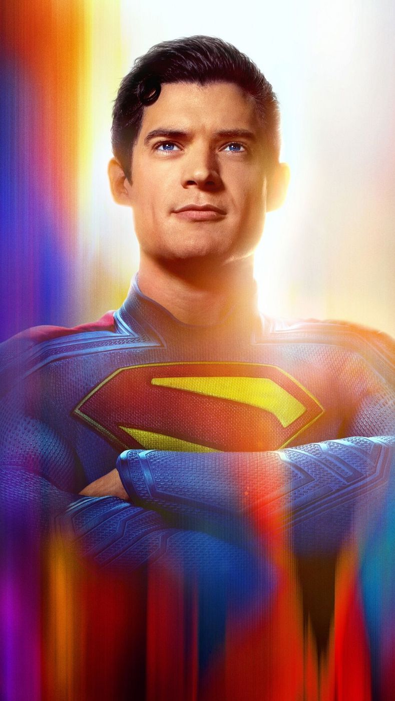 Superman, con traje clásico, posa con los brazos cruzados sobre un fondo abstracto con tonos rojos, naranjas, azules y violetas.