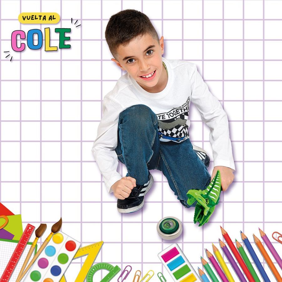 Niño sonriente jugando con un dino-lanzador de peonzas, rodeado de útiles escolares en un fondo cuadriculado.  Escena festiva de vuelta al cole.