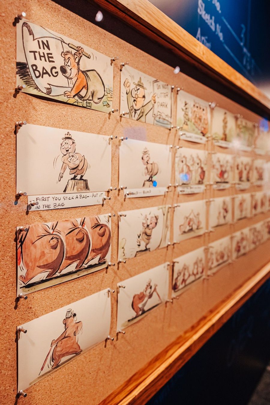 Storyboard de la animación "In the Bag" (1956) que muestra dibujos de un oso marrón y un guardabosques, con textos como "IN THE BAG" y "DO NOT LITTER PARK", fijados a un panel de corcho.