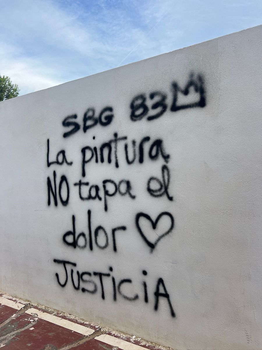 Un mural en una pared blanca presenta grafitis en negro, incluyendo "SBG 83M" con una corona, la frase "La pintura NO tapa el corazón" y la palabra "Justicia".