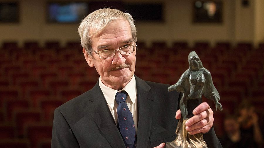 Stanislav Petrov, con traje oscuro y corbata, sostiene el Premio Dresden, una estatuilla femenina, en un auditorio con asientos rojos.