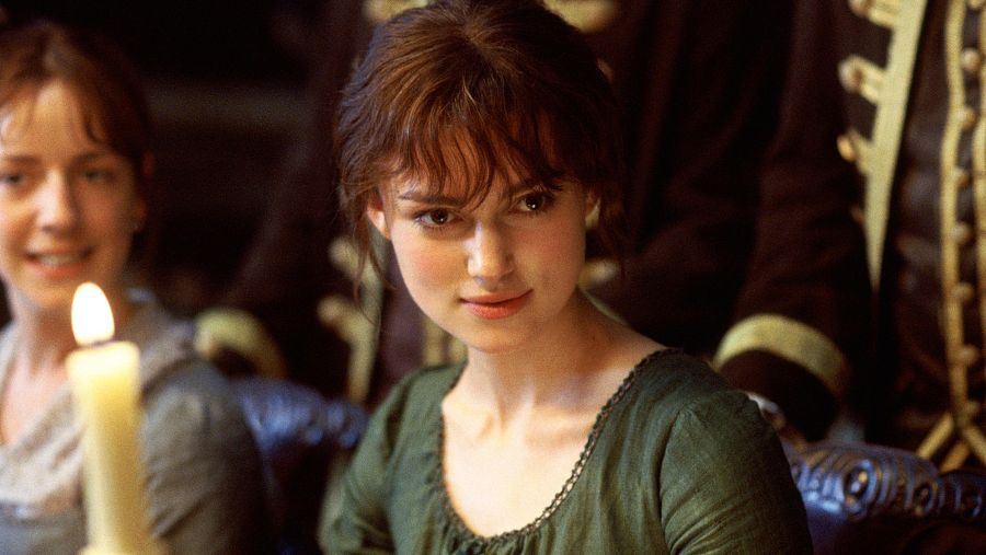 Keira Knightley, como Elizabeth Bennet, luce un vestido verde en una escena iluminada por una vela, acompañada por otras dos figuras vestidas con ropa de época.