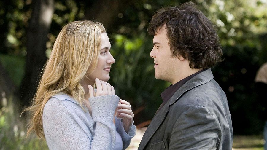 Kate Winslet y Jack Black protagonizan una escena de 'The Holiday', donde se les ve en un entorno natural. Kate, con cabello rubio y suéter claro, interactúa con Jack, quien lleva una chaqueta oscura.