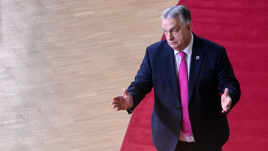 Viktor Orban, primer ministro húngaro, camina sobre una alfombra roja, vistiendo un traje oscuro con corbata rosa, mientras gesticula con las manos.