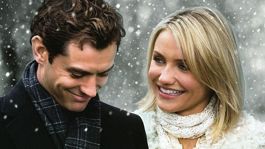 En una escena nevada de 'The Holiday', Jude Law, con abrigo oscuro y bufanda, sonríe. Cameron Díaz, con un chaleco blanco, también muestra una sonrisa.