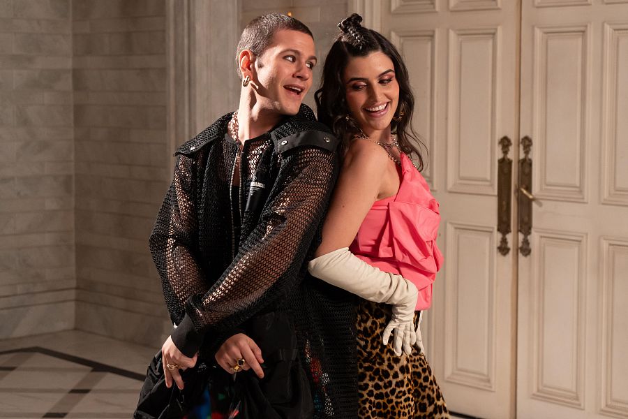 Rafa Álamos y Loren Mairena, sonriendo, posan juntos. Él lleva una chaqueta de malla y ella un top rosa con falda estampada. Ambos visten complementos plateados.