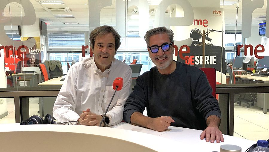 Dos hombres, Paco Grande y Arturo Martín, posan sonrientes en un estudio de radio. Uno viste camisa blanca y el otro un jersey oscuro con gafas. Un micrófono rojo con el logo de la emisora y unos auriculares se encuentran sobre la mesa.