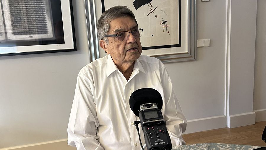 Sergio Ramírez, con gafas y camisa blanca, se encuentra frente a un micrófono. Detrás de él, una pared gris con dos obras de arte.