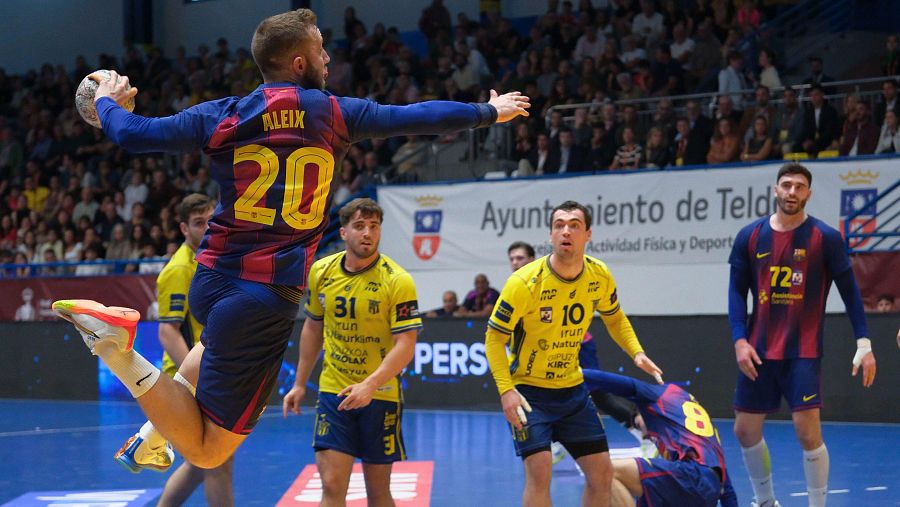 Un jugador con la camiseta número 20 y el nombre "ALEIX" salta para lanzar el balón en un partido de balonmano. Se enfrentan dos equipos, uno con camisetas azulgranas y otro con camisetas amarillas, en un pabellón deportivo con público.