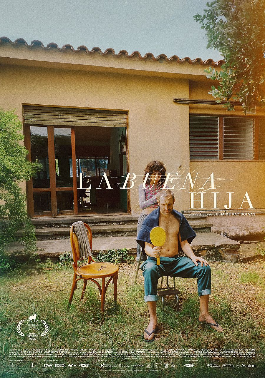 Un hombre sin camisa, con una toalla azul y sandalias, se refleja en un espejo amarillo que sostiene en un jardín. Una mujer observa la escena, mientras que una casa con puerta de cristal y ventanas con persianas sirve de fondo.