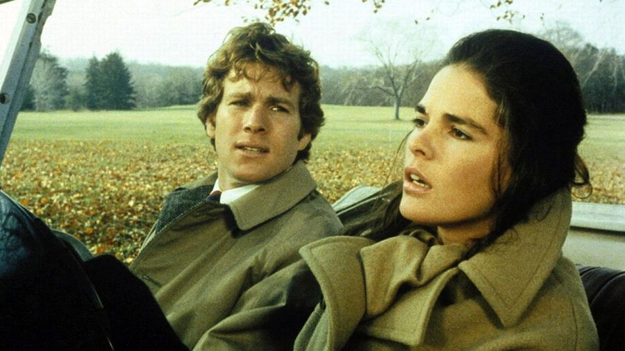 Una fotografía de Ali MacGraw y Ryan O'Neal, ambos vestidos con abrigos, posando en un entorno otoñal con árboles y hojas caídas, creando una atmósfera romántica.