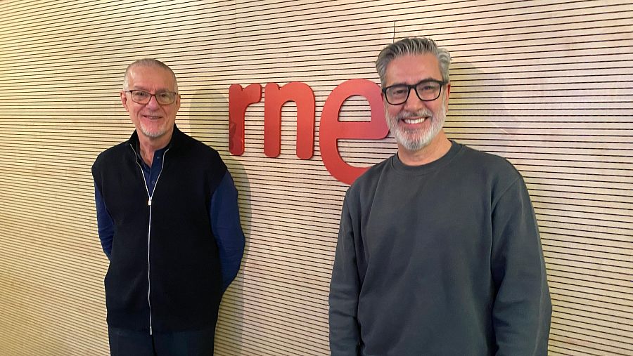 Dos hombres, Vicente Andrés García y Arturo Martín, posan sonriendo en un estudio de radio. Uno lleva camisa azul y chaleco negro, el otro un suéter gris oscuro. Al fondo, se distingue el logotipo de la emisora.