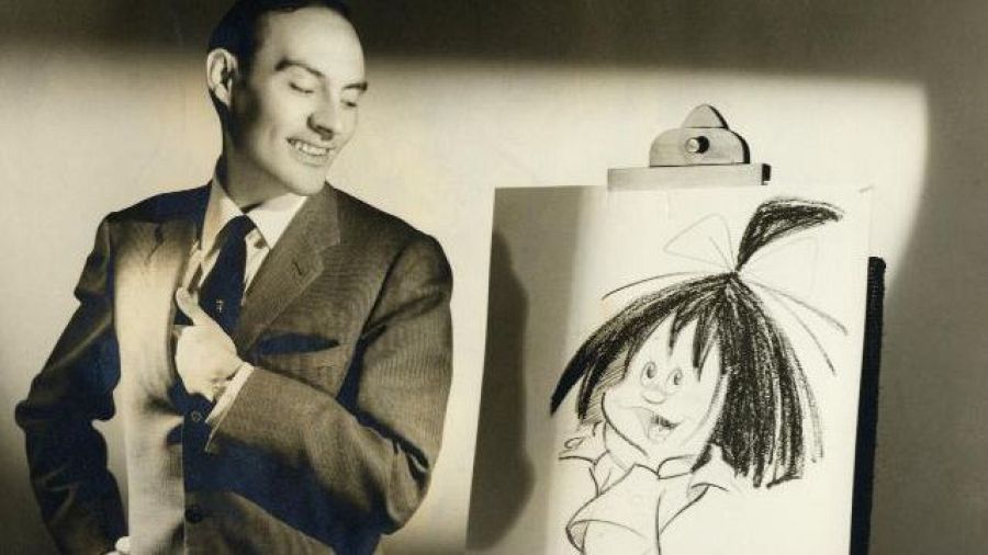José Luis Moro, vestido formalmente, posa junto a un caballete que exhibe un dibujo infantil. La obra retrata a una niña con un lazo y la lengua afuera, capturando una expresión traviesa.