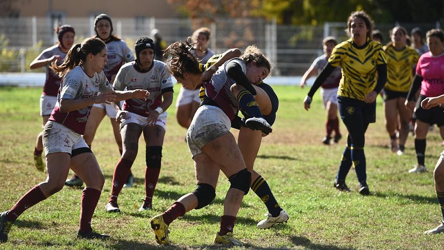 En la imagen se puede observar a un grupo de mujeres jugando al rugbi en un campo de cesped