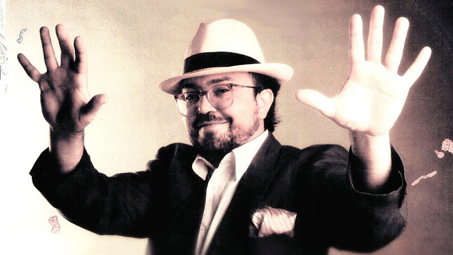 Xavier Patricio Pérez Álvarez, "Gato Pérez", posa con un sombrero claro y gafas, vistiendo una chaqueta oscura sobre una camisa blanca, con las manos levantadas en un fondo sepia.