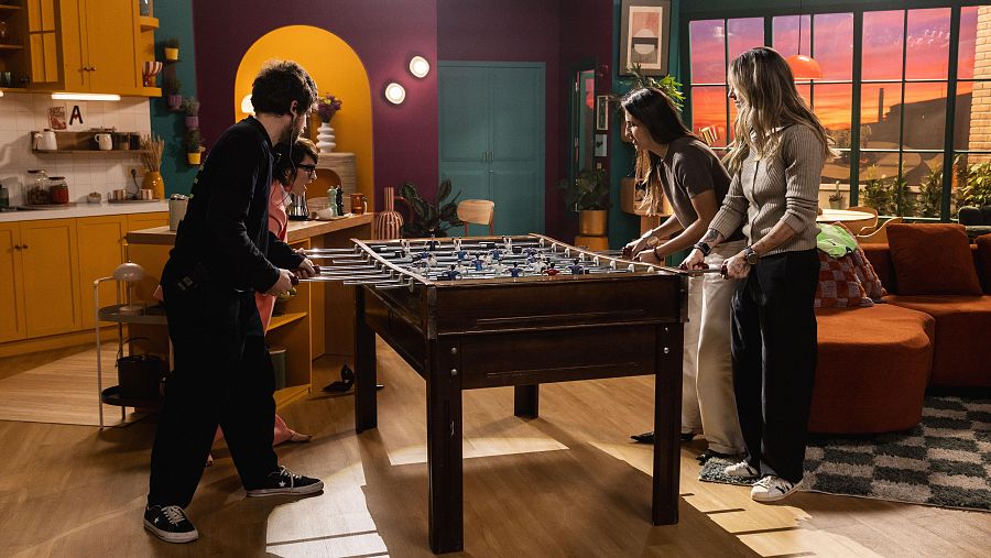 Sílvia Abril, Kika Nazareth y Mapi León juegan al futbolín en un set de TV. La imagen muestra un ambiente moderno y colorido con elementos de cocina y salón.