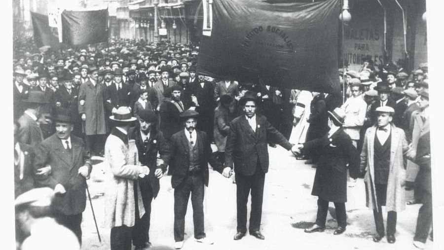 Multitudinaria manifestación del 1º de mayo de 1920 en Madrid, con Pablo Iglesias Posse al frente. Se observa una pancarta con "PARTIDO SOCIALISTA" y edificios urbanos.