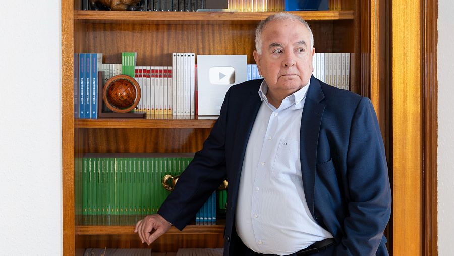 Antoni Bolinches, psicólogo, posa de medio cuerpo frente a una estantería con libros, un globo terráqueo y una placa de YouTube. Viste camisa azul y americana azul marino.
