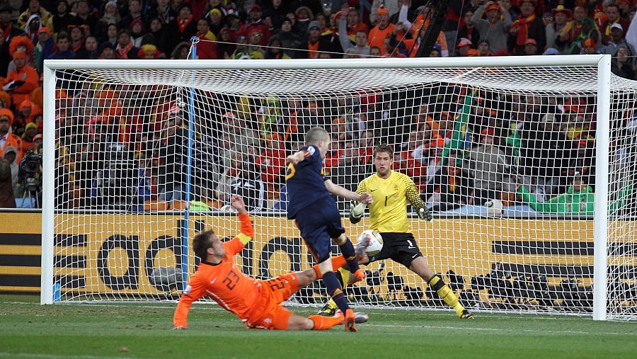 Andrés Iniesta anota un gol con el pie derecho. El portero Maarten Stekelenburg y Rafael van der Vaart intentan detener el balón. El balón está cerca de la red.