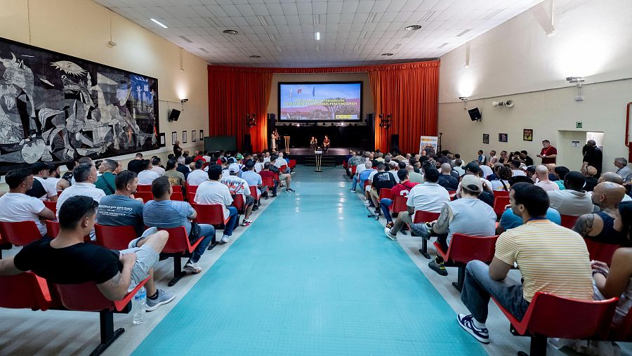 Salón de eventos con audiencia y escenario. Destaca un mural monocromático y sillas rojas. Coloquio sobre 'Sorda' en el Centro Penitenciario Madrid IV.