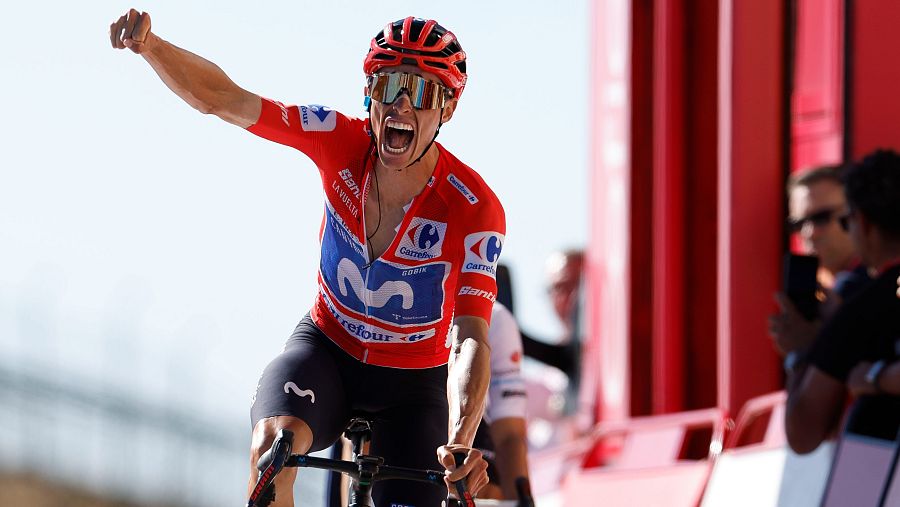 Enric Mas, ciclista del Movistar, celebra con el puño en alto y una expresión de euforia. Su maillot luce los logos de Movistar, Carrefour y La Vuelta.