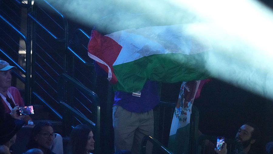 Un manifestante muestra las banderas mexicana y palestina durante el discurso de JD Vance