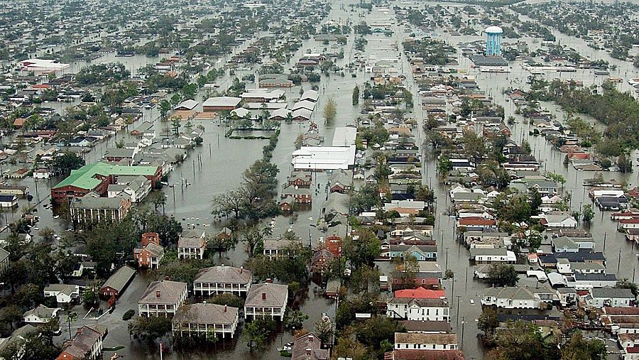 Vista aérea de una zona urbana inundada, con casas y árboles sumergidos. Una torre de agua azul es visible en medio de la devastación.