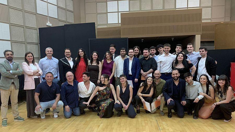 Fotografía de grupo de graduados en un auditorio, con Ignacio Elguero de RTVE presente. Los asistentes sostienen diplomas naranjas.