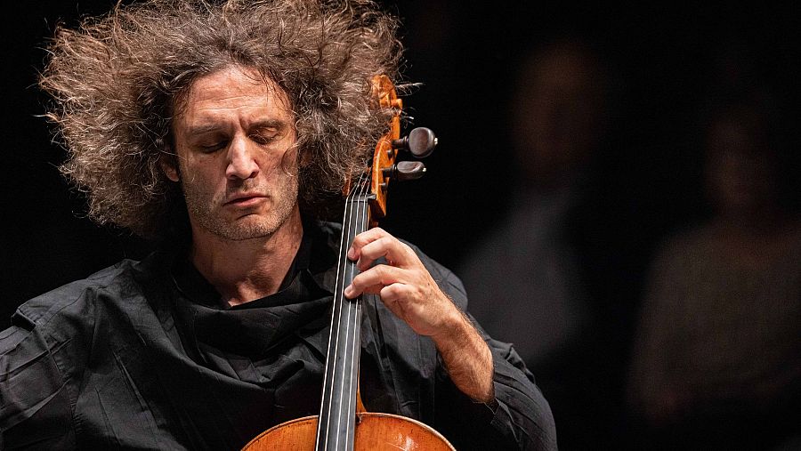 El violonchelista Nicolas Altstaedt toca concentrado su instrumento en un plano medio con iluminación cenital sobre fondo oscuro.