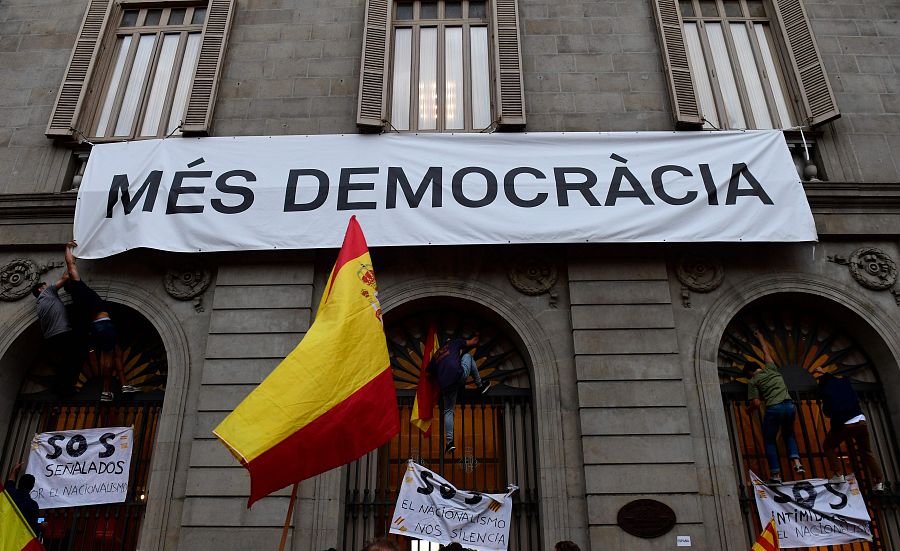 Manifestantes intentan descolgar una pancarta en la que pone "Más democracia", en la plaza de Sant Jaume, en Barcelona