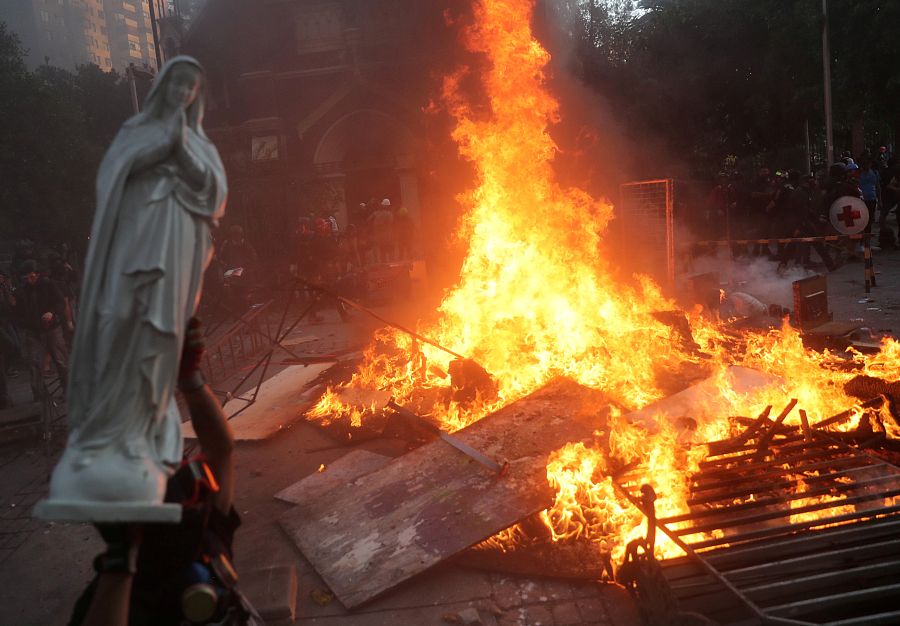 Un manifestante sostiene una estatua de la Virgen María frente a una barricada ardiendo en Santiago, enero de 2020