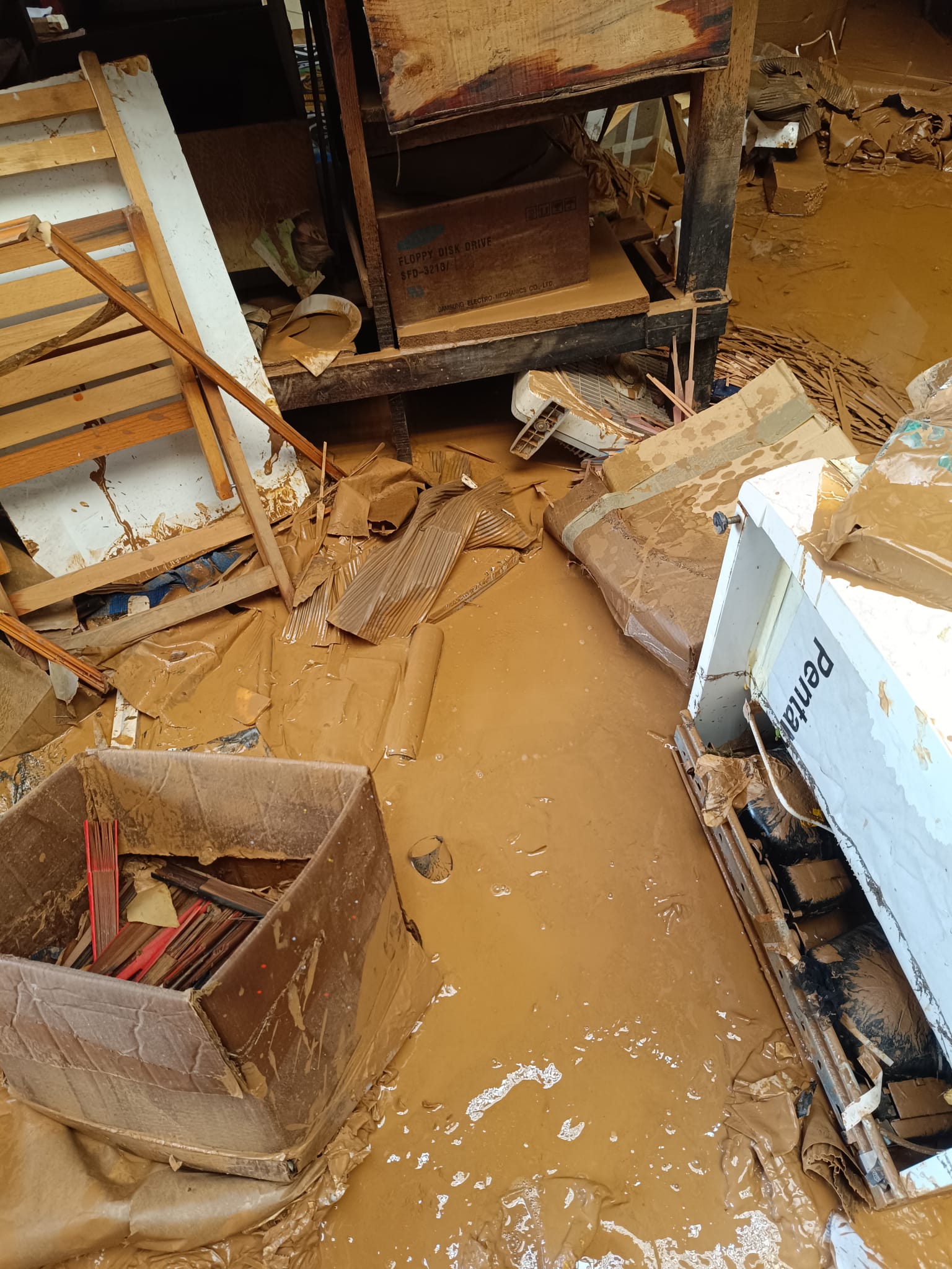 Así quedó el taller de Abanicos Andrés tras la dana del 29 de octubre | Fotos cedidas por Macarena Andrés Un taller inundado revela el desastre: agua turbia y barro cubren el suelo y los objetos, incluyendo cajas, un mueble y una nevera, sugiriendo la magnitud de la inundación.