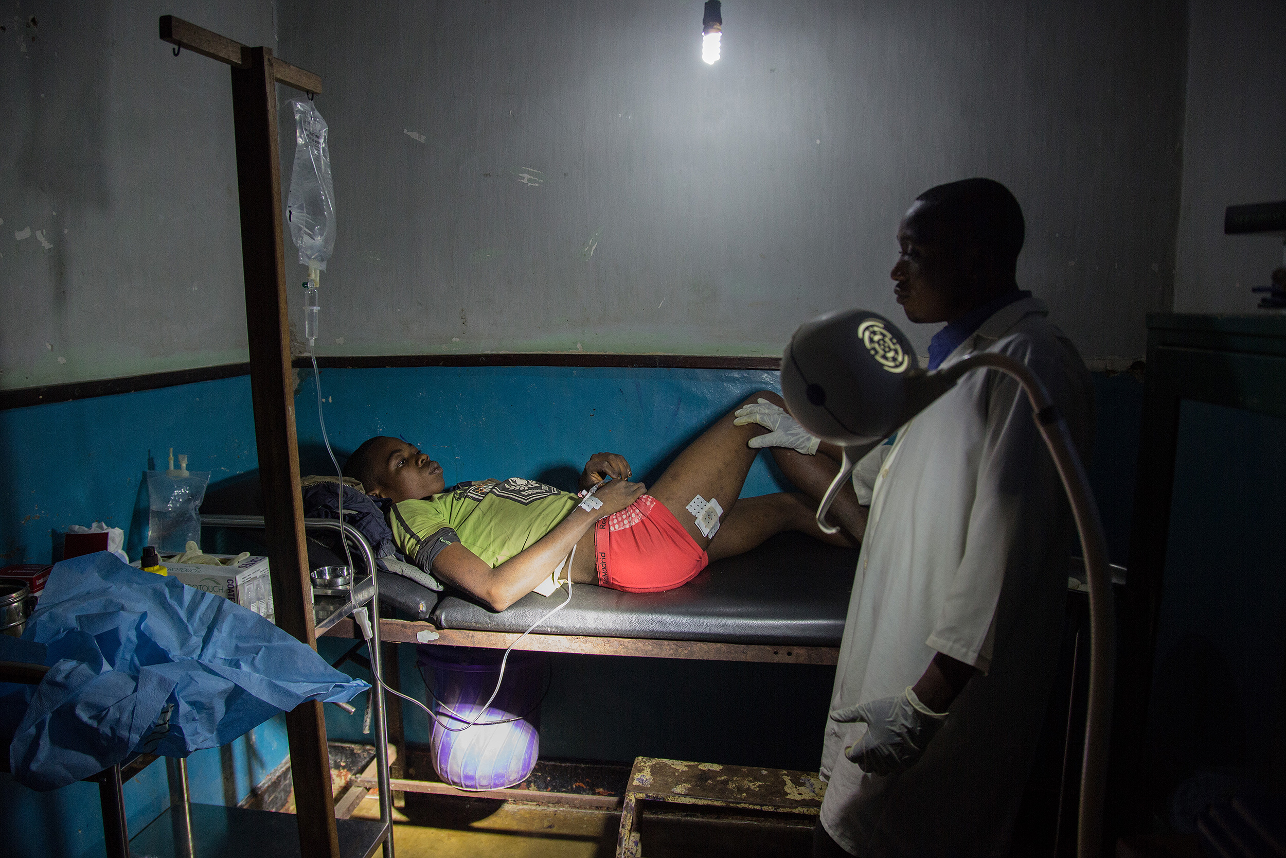 Un joven yace en una cama del hospital de Lulingu, bajo la supervisin de un mdico. Luce un vendaje en una de sus piernas.