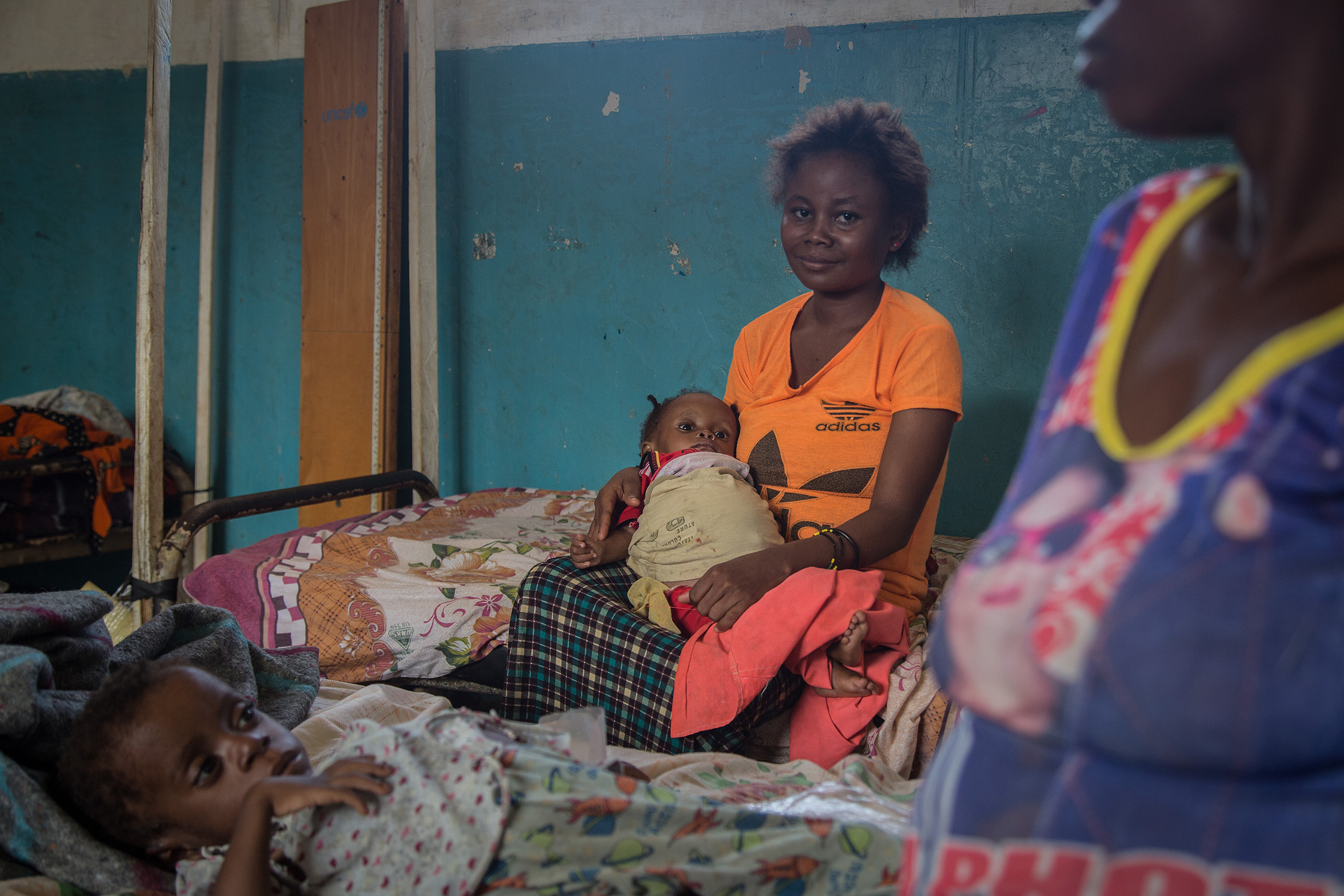 Una mujer con una camiseta naranja espera sentada en la cama del hospital de Lulingu con su hijo en brazos.
