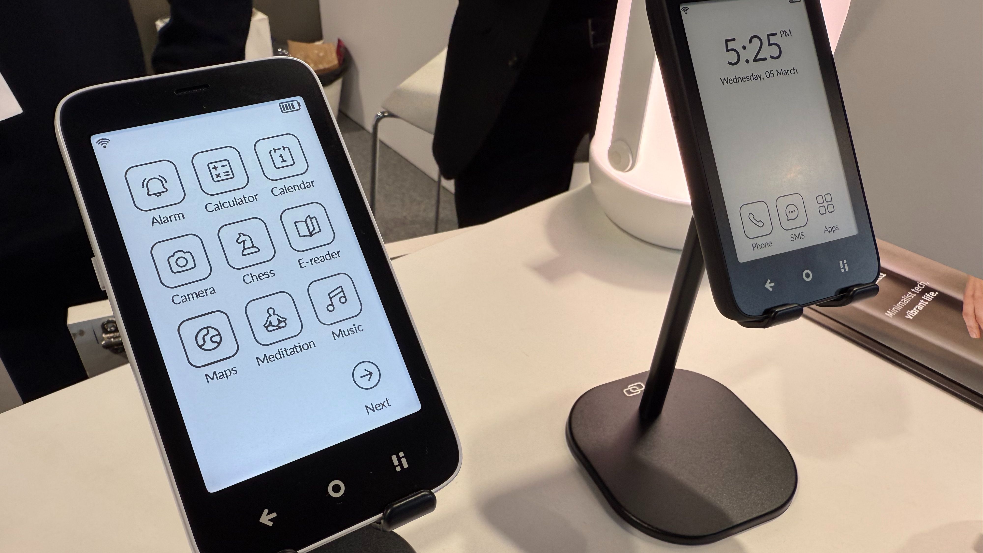 Teléfonos minimalistas con pantallas de tinta electrónica muestran interfaces sencillas: uno con iconos de aplicaciones y otro con hora y opciones de llamada, SMS y apps.