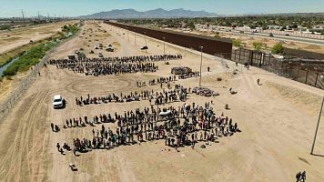 Cientos de migrantes mientras esperan junto al muro fronterizo en El Paso, en Texas, EE.UU.