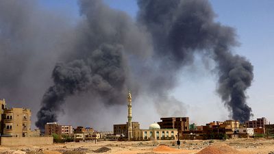 Un hombre camina mientras se eleva humo sobre los edificios tras un bombardeo areo en Jartum Norte