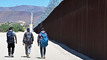 Varios migrantes caminan por el lado estadounidense del muro fronterizo en Jacumba Hot Springs, California, tras cruzar a pie desde Mxico.