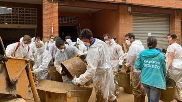 Un grupo de voluntarios vierte capazos de lodo sobre la pala de un tractor