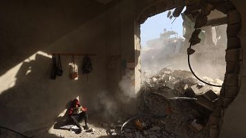 Un niño palestino sostiene un libro mientras está sentado entre los escombros de una casa