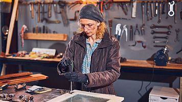 Woman carpenter sanding old window in a retro workshop.