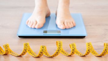 Tape measure and woman feet standing on weigh scales.Diet, weight loss and feet of a woman on a scale for body check, measure and balance to lose weight on the floor. Obesity, scales and girl with tape
