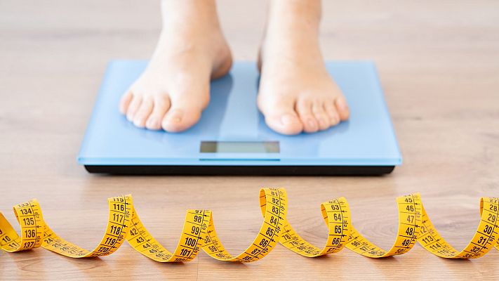Tape measure and woman feet standing on weigh scales.Diet, weight loss and feet of a woman on a scale for body check, measure and balance to lose weight on the floor. Obesity, scales and girl with tape