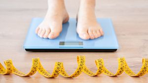 Tape measure and woman feet standing on weigh scales.Diet, weight loss and feet of a woman on a scale for body check, measure and balance to lose weight on the floor. Obesity, scales and girl with tape