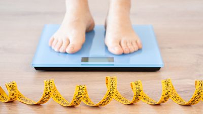 Tape measure and woman feet standing on weigh scales.Diet, weight loss and feet of a woman on a scale for body check, measure and balance to lose weight on the floor. Obesity, scales and girl with tape