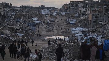 Palestinos caminan junto a edificios destruidos en el norte de la Franja de Gaza, ayer dos de enero.